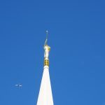 A plane flies by the spire of the Jordan River Temple.