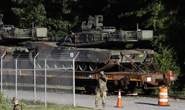 Military police walk near Abrams tanks on a flat car in a rail yard, Monday, July 1, 2019, in Washi...