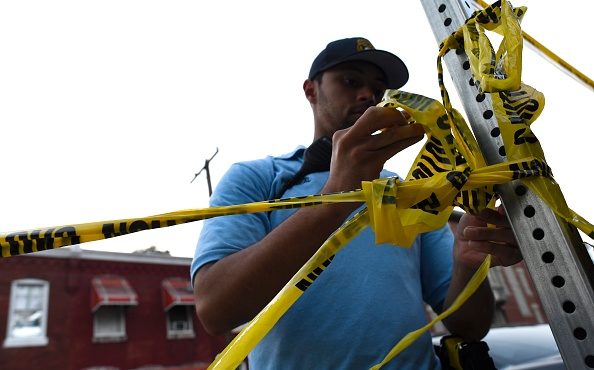 A police officer ties tape to a post for crowd control while responding to a shooting on August 14,...