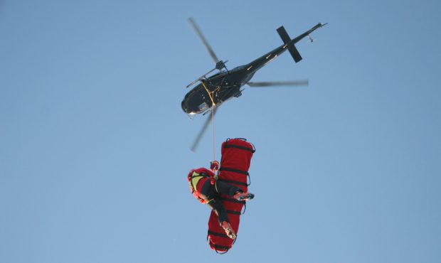 A rescue worker flies undr a helicopter with a patient in a rescue stretcher....