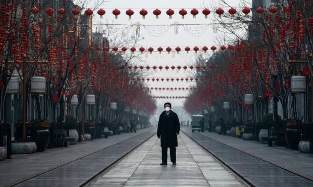 A Chinese man wears a protective mask as he walks in a nearly empty and shuttered commercial street...