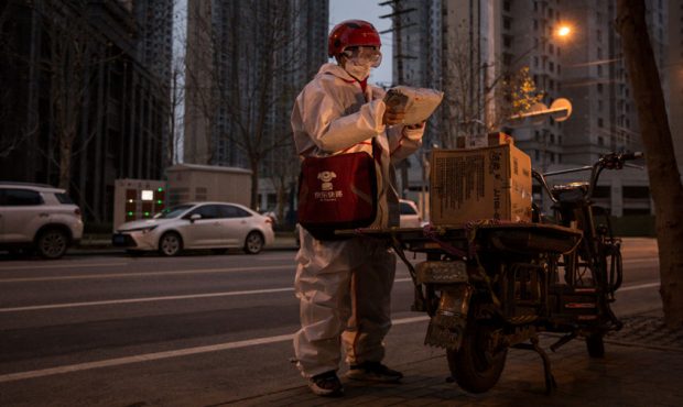 An expressman wears a protective mask and suit as he delivers packages on a bicycle on February 1, ...
