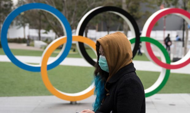 TOKYO, JAPAN - FEBRUARY 26: A woman wearing a face mask walks past the Olympic rings in front of th...