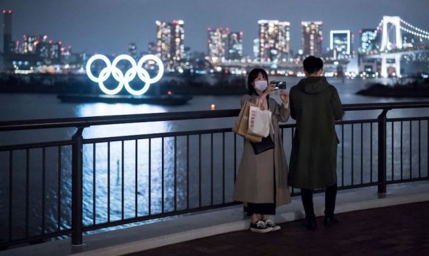 A woman wearing a face mask uses a smartphone as she takes a photograph in front of the Olympic rin...