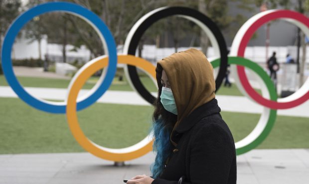 A woman wearing a face mask walks past the Olympic rings in front of the new National Stadium, the ...