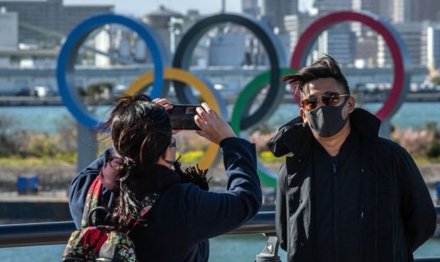 A man wearing a face mask has his photograph taken in front of the Olympic Rings in Odaiba on March...