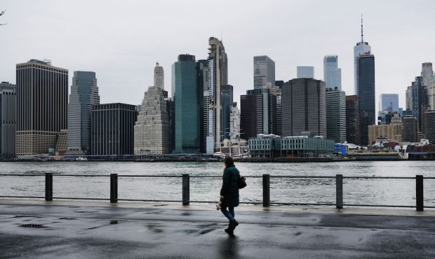 People walk in Brooklyn while lower Manhattan looms in the background on March 28, 2020 in New York...