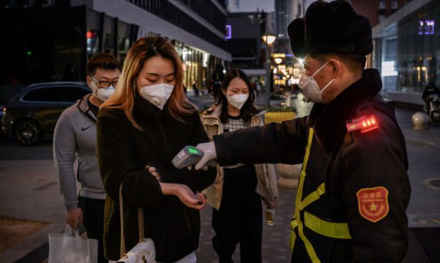 A Chinese woman wears a protective mask as she has her temperature checked by a security guard befo...