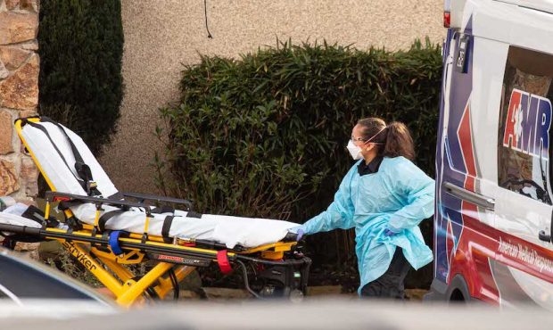 A healthcare worker prepares to transport a patient on a stretcher into an ambulance at Life Care C...