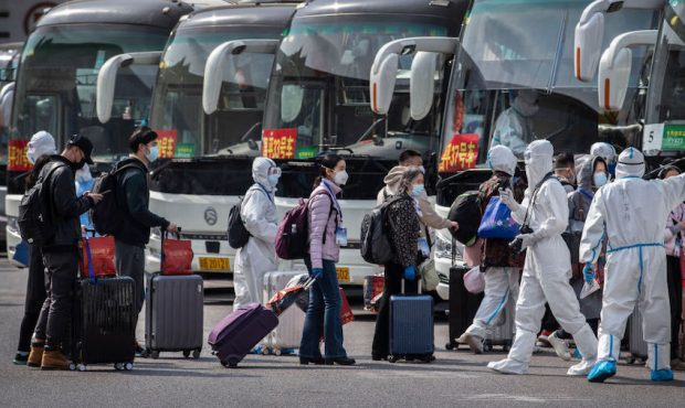 Chinese workers and health officials wear protective white suits as travellers from Wuhan gather to...