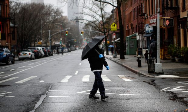 A pedestrian wearing a protective mask and protective gloves walks across an empty Dekalb Avenue, S...