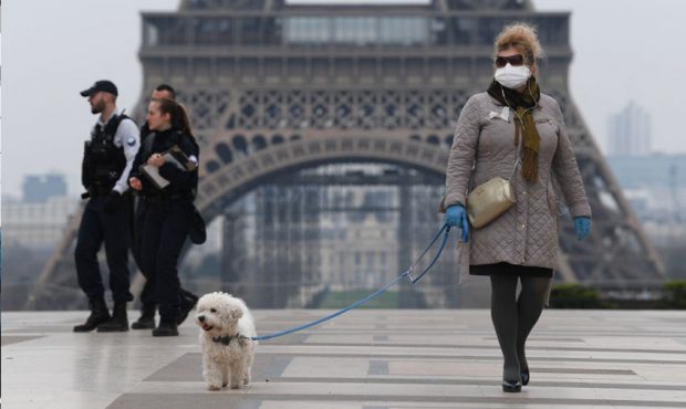 A woman wearing a protective mask walks her dog on the Esplanade du Trocadero square in front of th...