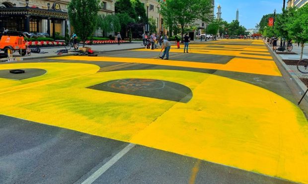 Giant, yellow letters are painted on a busy Washington D.C. street spelling out "BLACK LIVES MATTER...