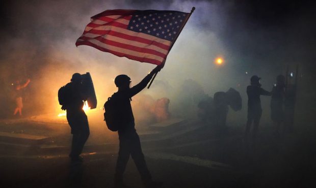 A protester flies an American flag while walking through tear gas fired by federal officers during ...