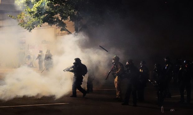 PORTLAND, OR - JULY 21: Federal officers walk through tear gas while dispersing a crowd of about a ...