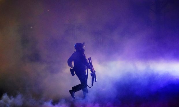 A federal officer runs through tear gas while dispersing a crowd of about a thousand protesters in ...