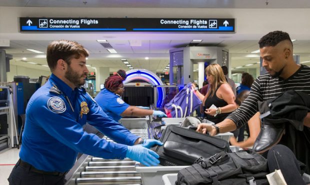 Transportation Security Administration (TSA) agents help travelers place their bags through the 3-D...