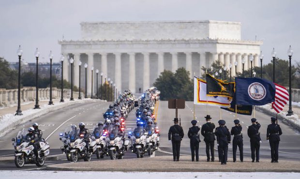 Police officers riding on motorcycles approach Arlington National Cemetery during the funeral proce...