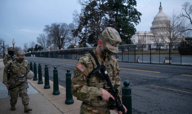 Members of the National Guard walk by the fenced perimeter that surrounds the U.S. Capitol in the e...