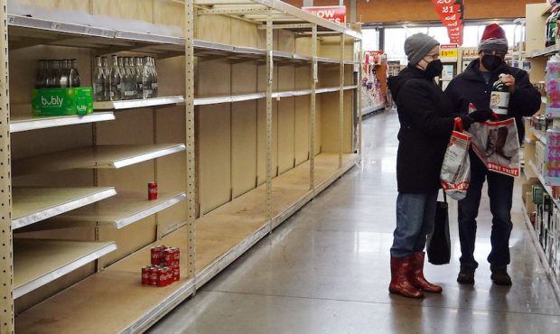 An empty water bottle shelf is bare as people stock up on necessities at the H-E-B grocery store on...