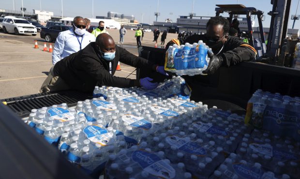 Volunteers load cases of water into the bed of a truck during a mass water distribution at Delmar S...