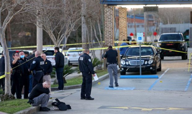 A man sits on the curb inside the crime scene tape in the parking lot of the Jefferson Gun Outlet a...