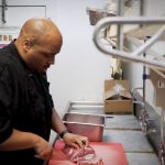 Chef Julius Thompson cuts meat in the back of his restaurant, "Sauce Boss Southern Kitchen."