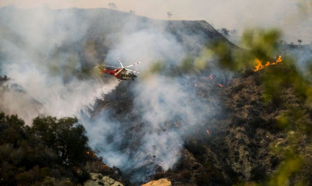 A firefighting helicopter drops water on a brush fire scorching of an area west of Los Angeles Satu...