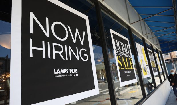 A pedestrian walks by a Now Hiring sign outside of a Lamps Plus store on June 03, 2021 in San Franc...