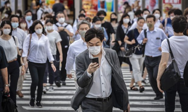 A man wearing a face mask cross a street as he checks his phone on August 05, 2021 in Tokyo, Japan....