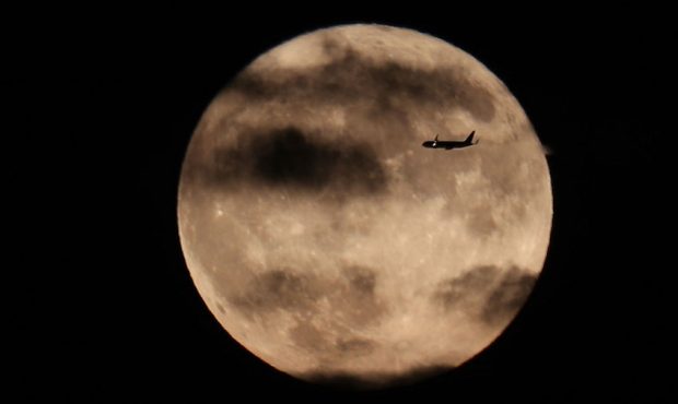A plane flies past the harvest moon as it rises behind the Statue of Liberty in New York City, on O...