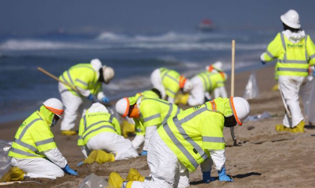 Cleanup workers in protective suits work along the contaminated Huntington State Beach, which is cl...