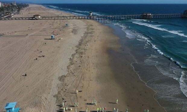 In an aerial view, cleanup workers (BOTTOM) search for contaminated sand and seaweed, with a few be...