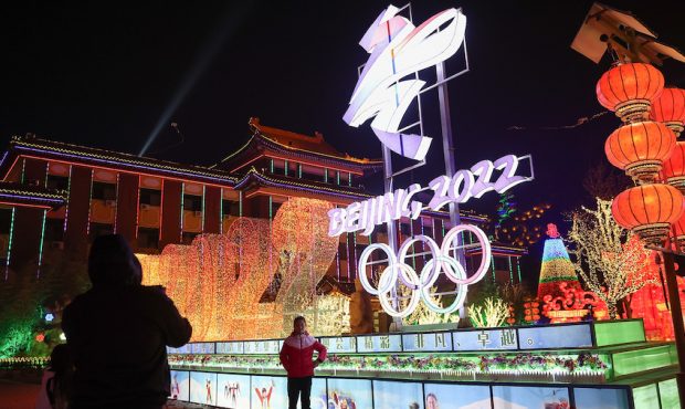 FILE: People wear protective masks as they walk front the logos of the 2022 Beijing Winter Olympics...