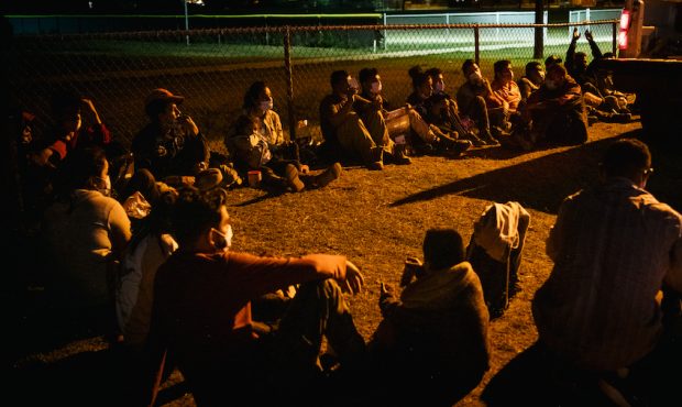 Migrants sit together while waiting to board a border patrol bus after crossing the Rio Grande into...