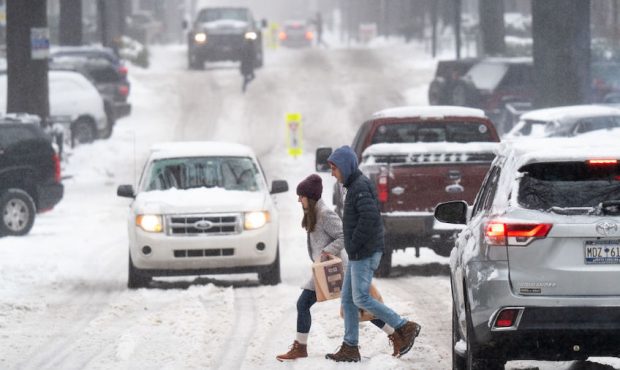 Pedestrians cross a street as motorists drive through the snow on January 16, 2022 in Greenville, S...