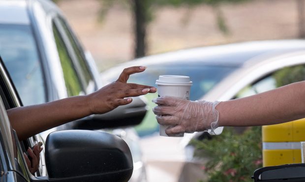 A Starbucks Corp. employee wearing protective gloves hands a customer an order from a drive-thru wi...