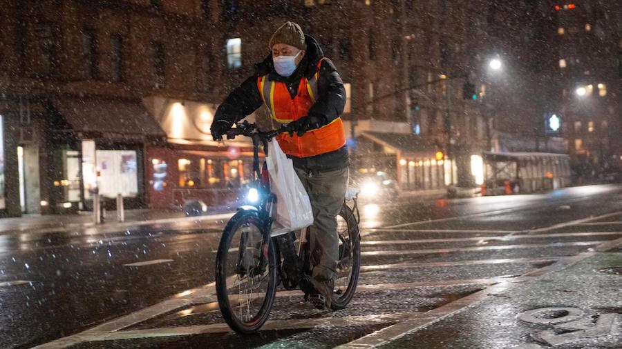 A food delivery driver on a bicycle rides in the snow on Friday in New York City. (Alexi Rosenfeld/...