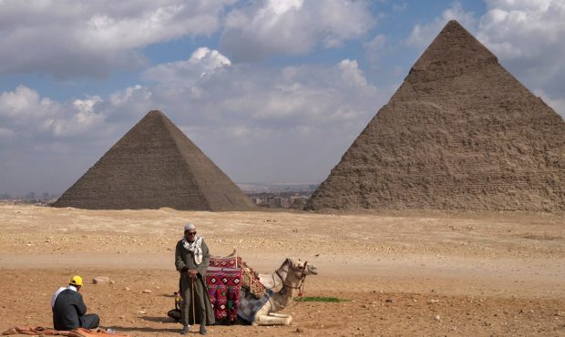 A picture taken on December 17, 2021 shows men resting next to a camel with the Great Pyramid of Kh...