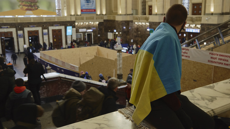 A man wearing the Ukrainian national flag is waiting for a train at the train station as all trains...