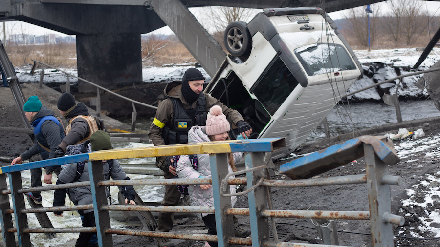 A Ukrainian serviceman help a child to cross the destroyed bridge on March 1, 2022 in Irpin, Ukrain...