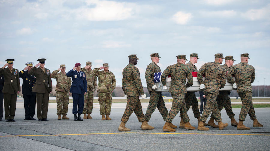 Military officials salute as a U.S. Marine Corps carry team carries the transfer case containing th...