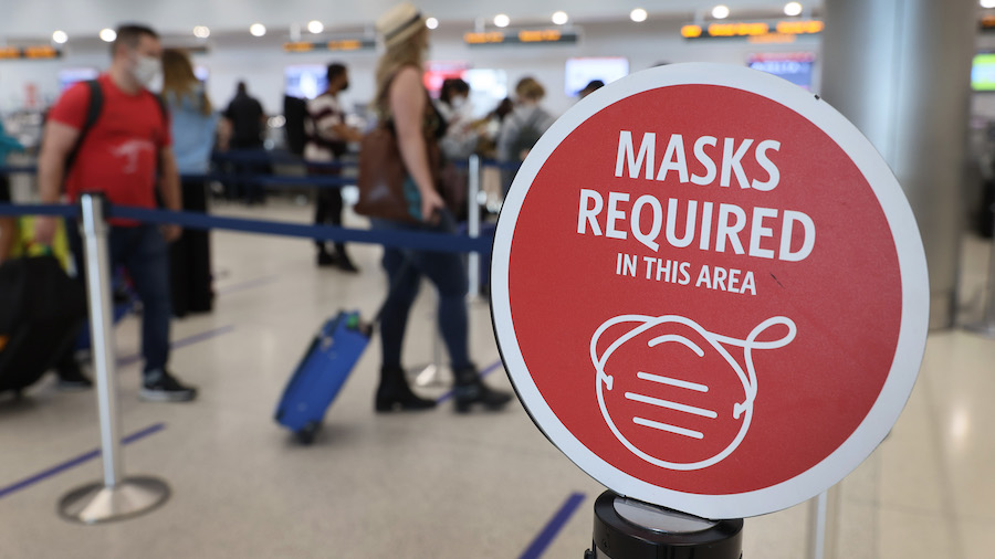 FILE: A sign reading, 'masks required in this area,' is seen as travelers prepare to check-in for t...
