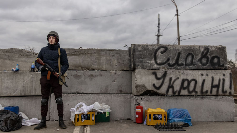 A member of a Territorial Defence unit guards a barricade next to writing saying " Glory To Ukraine...