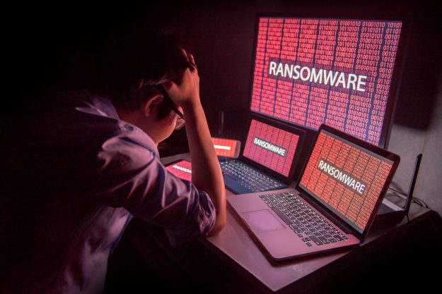 frustrated man in front of computer screens showing ransomware
