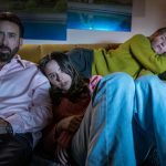 Nicolas Cage (“Nick Cage”, left), Lily Sheen (“Addy”, center) and Sharon Horgan (“Olivia”, right) lay together in the living room as they watch a movie in THE UNBEARABLE WEIGHT OF MASSIVE TALENT.