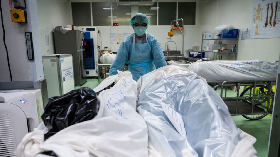 BANGKOK, THAILAND - JULY 28: A mortuary technician in PPE transfers sealed bags containing bodies s...