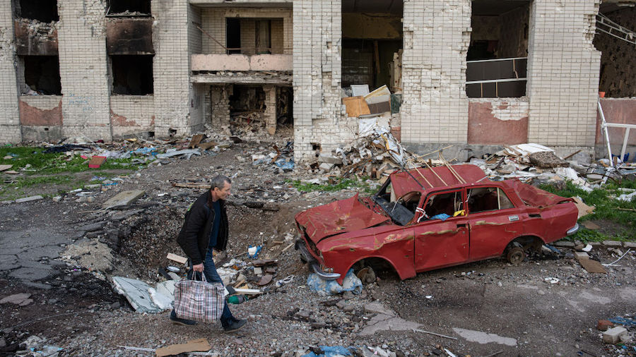 A man carries his belongings past a destroyed car next to a heavily damaged apartment building on M...