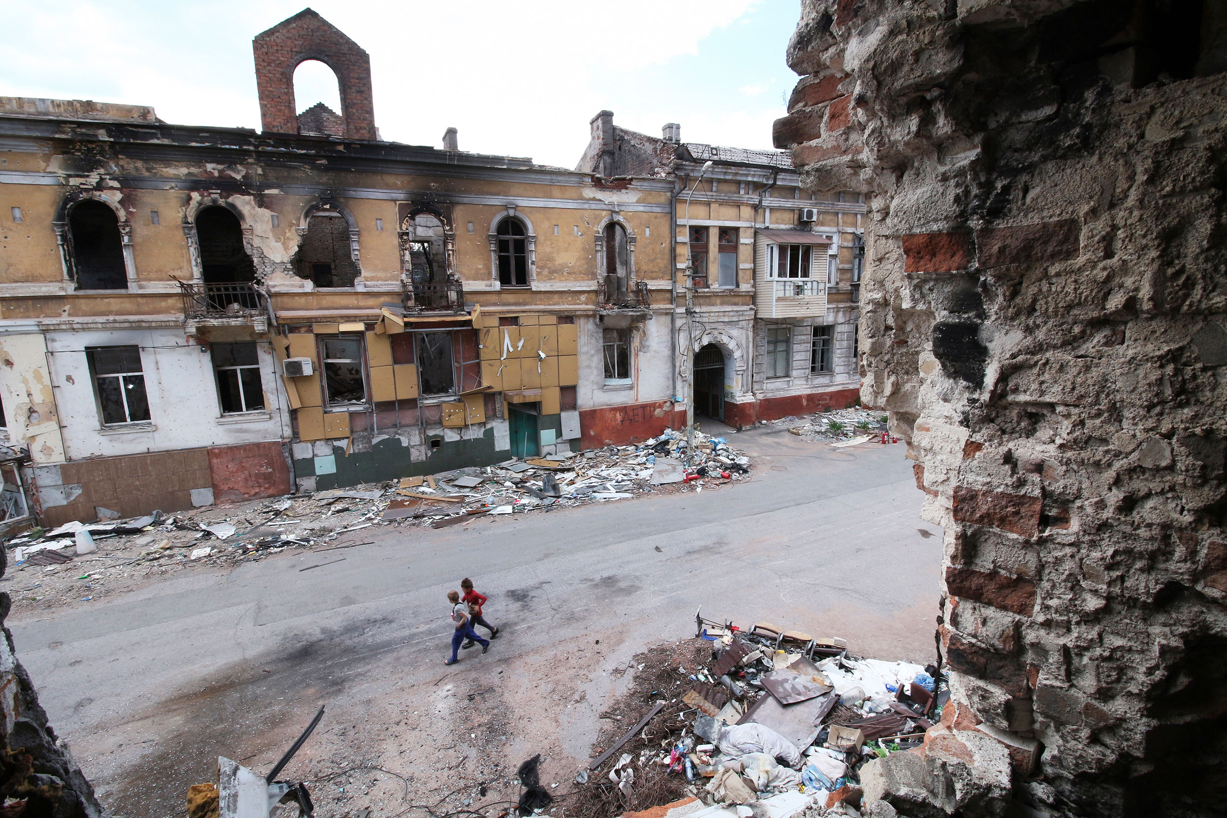 Children walk among buildings destroyed during fighting in Mariupol, in territory under the governm...