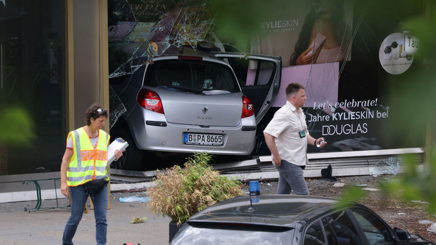 Police stand near a car that plowed into pedestrians and then smashed into a Douglas perfume store ...